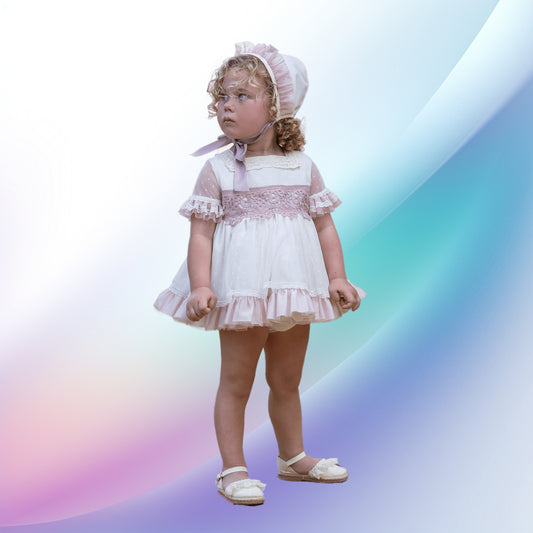 An elegant off-white and pale pink baby and toddler ceremony dress, perfect for a church event or baptism. Features include a lace-trimmed square neckline, a multilayered tulle skirt in pink and white, matching tulle-edged sleeves, and a lace bow at the back. Completing the ensemble are a tulle bonnet with a bow, and off-white knickers, all contributing to a harmonious, charming outfit.