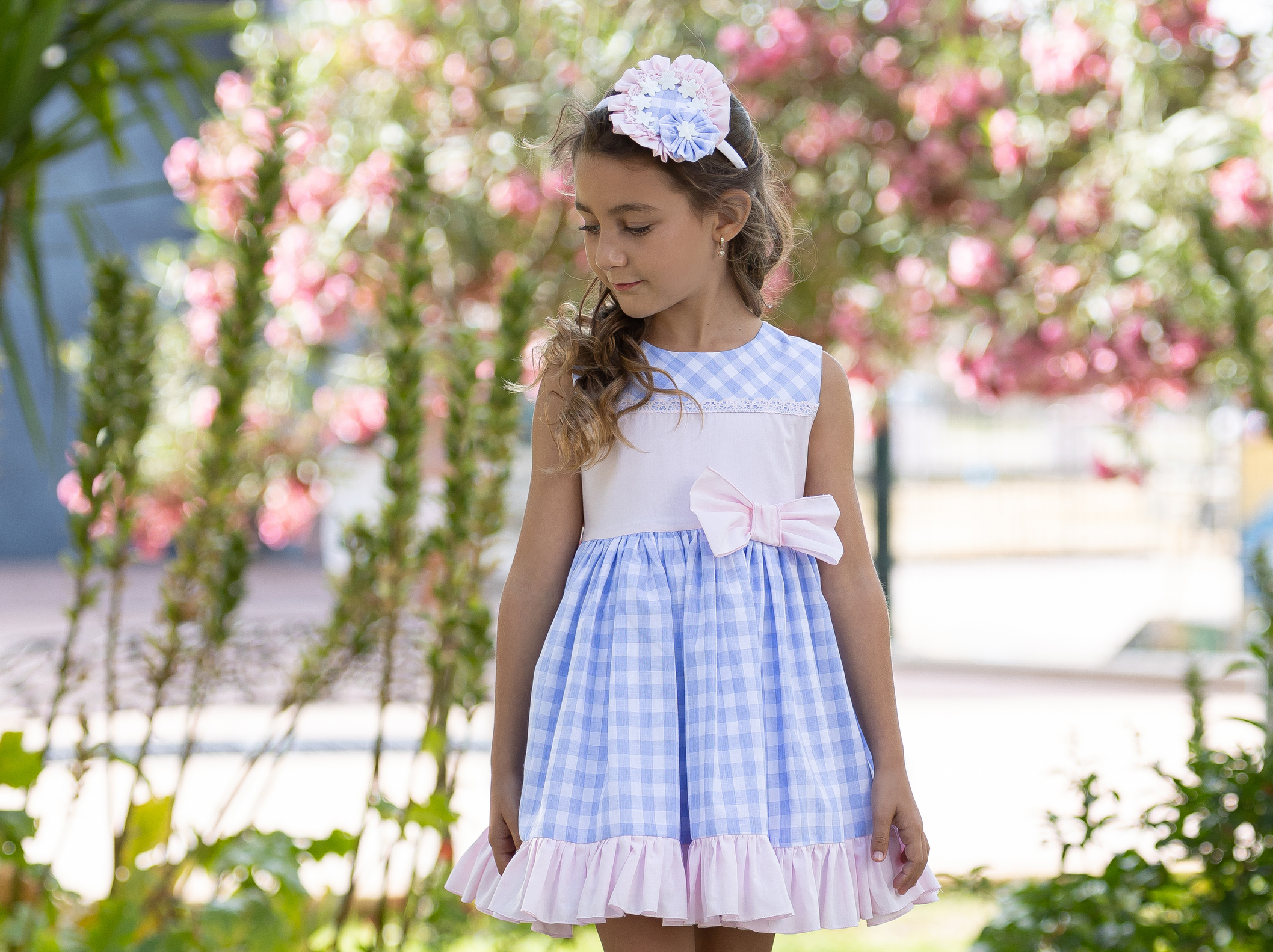 A charming little girl dons a stunning Spanish attire for a special occasion, her dress a harmonious blend of light blue and pink hues. The dress, showcasing traditional Spanish design elements, is beautifully complemented by intricate lace detailing. The light blue body of the dress contrasts with a voluminous pink tulle skirt, adding a vibrant pop of color. She stands poised, her attire exuding the elegance and cultural richness of Spain, making her the center of attention in this festive gathering.