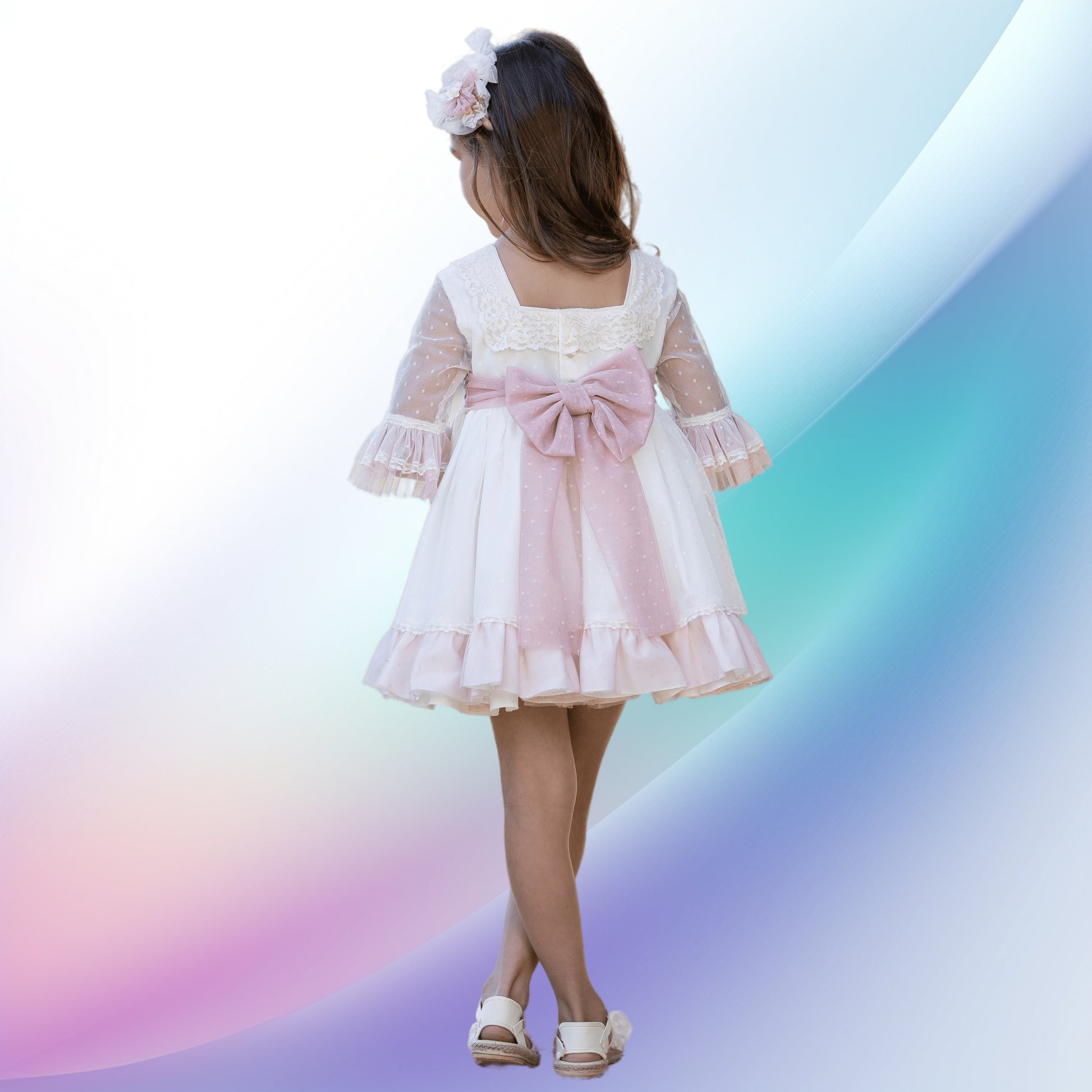 Image of an adorable off-white and pale pink girl's ceremony dress and diadem, perfect for weddings, church events, or first communions. The beautifully handcrafted dress features a lace-trimmed square neck, tulle sleeves, a multi-layered skirt with pink tulle, and a back bow. A matching flower-adorned headband completes this charming flower girl outfit.
