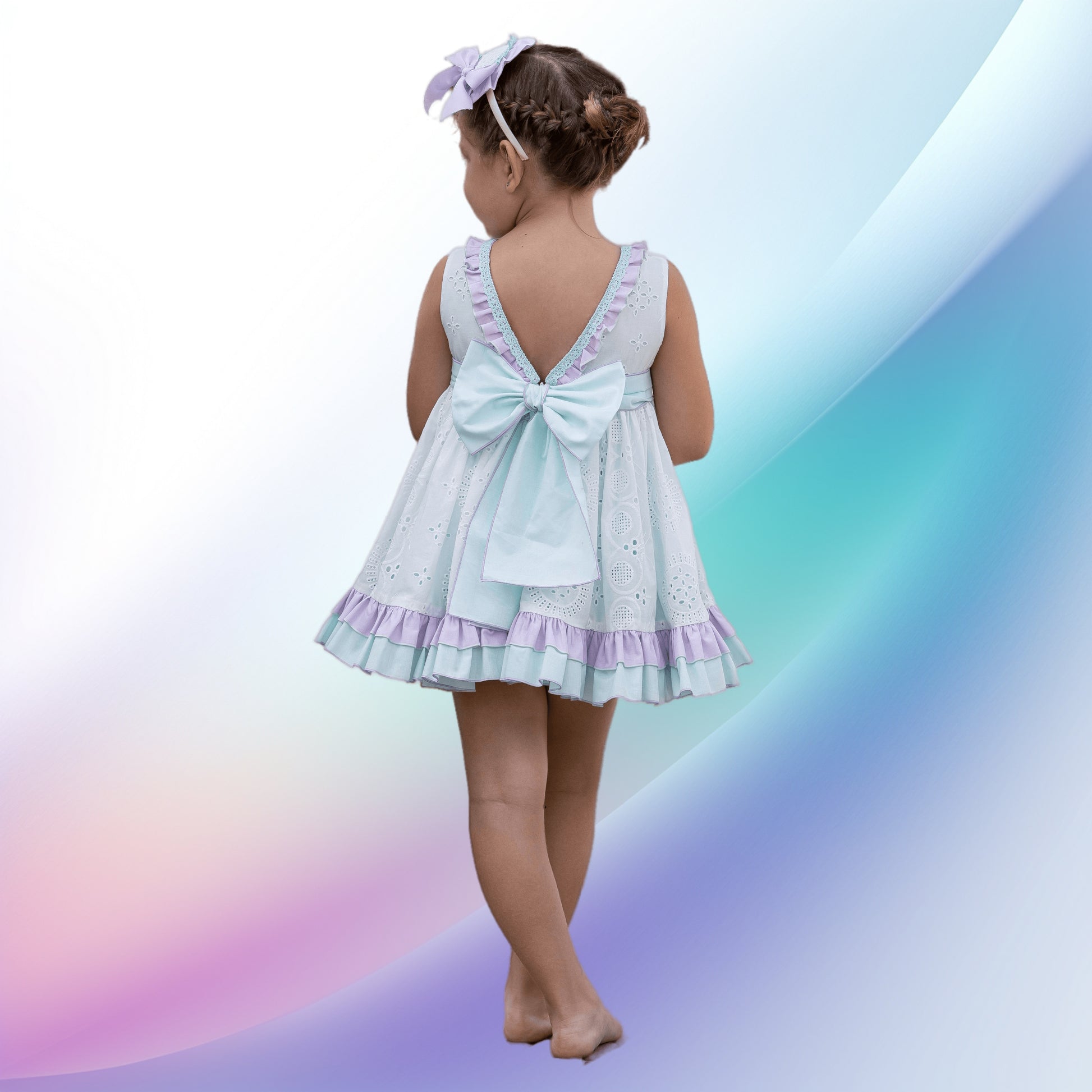 Image of a delightful pastel green and purple girl's dress and diadem by Abuela Tata. Perfect for weddings or parties, the dress features plumeti detailing, ruffle trim, and pearly pink back buttons. Crafted from a soft cotton-polyester blend, it is machine washable and ideal for a flower girl outfit.