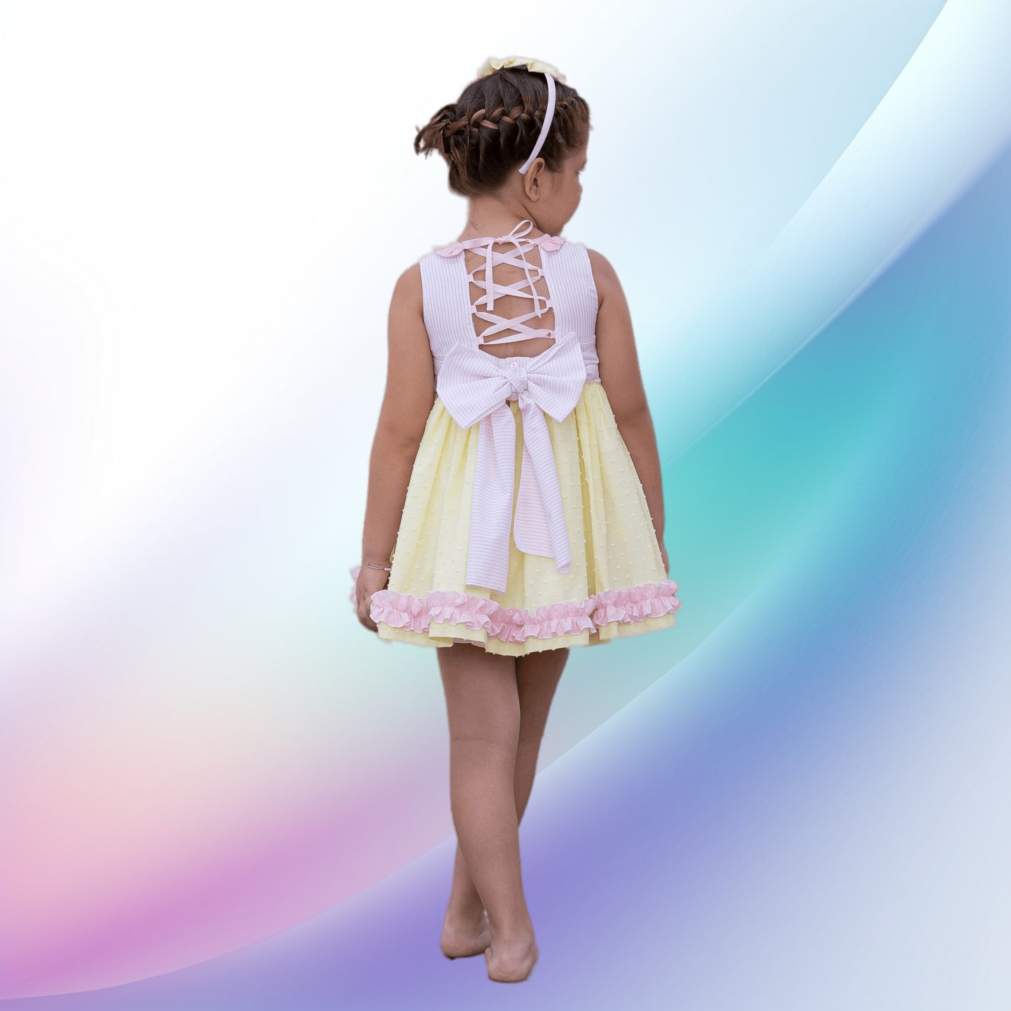 Image of a vintage yellow and pink dress, bonnet, and knickers set by Abuela Tata, perfect for a girl attending a party or wedding. The soft, lightweight, machine-washable outfit features charming ruffle trims, stripes, plumeti detailing, back button fastenings, and a fixed sash tie, making it an ideal flower girl dress.